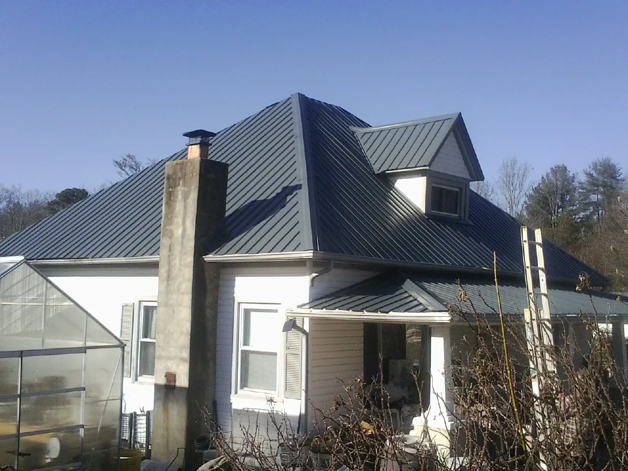 Dark blue standing seam metal roof on a white farmhouse with dormer — Slate & Tile Roof Repair by Roofing Brothers in Leo