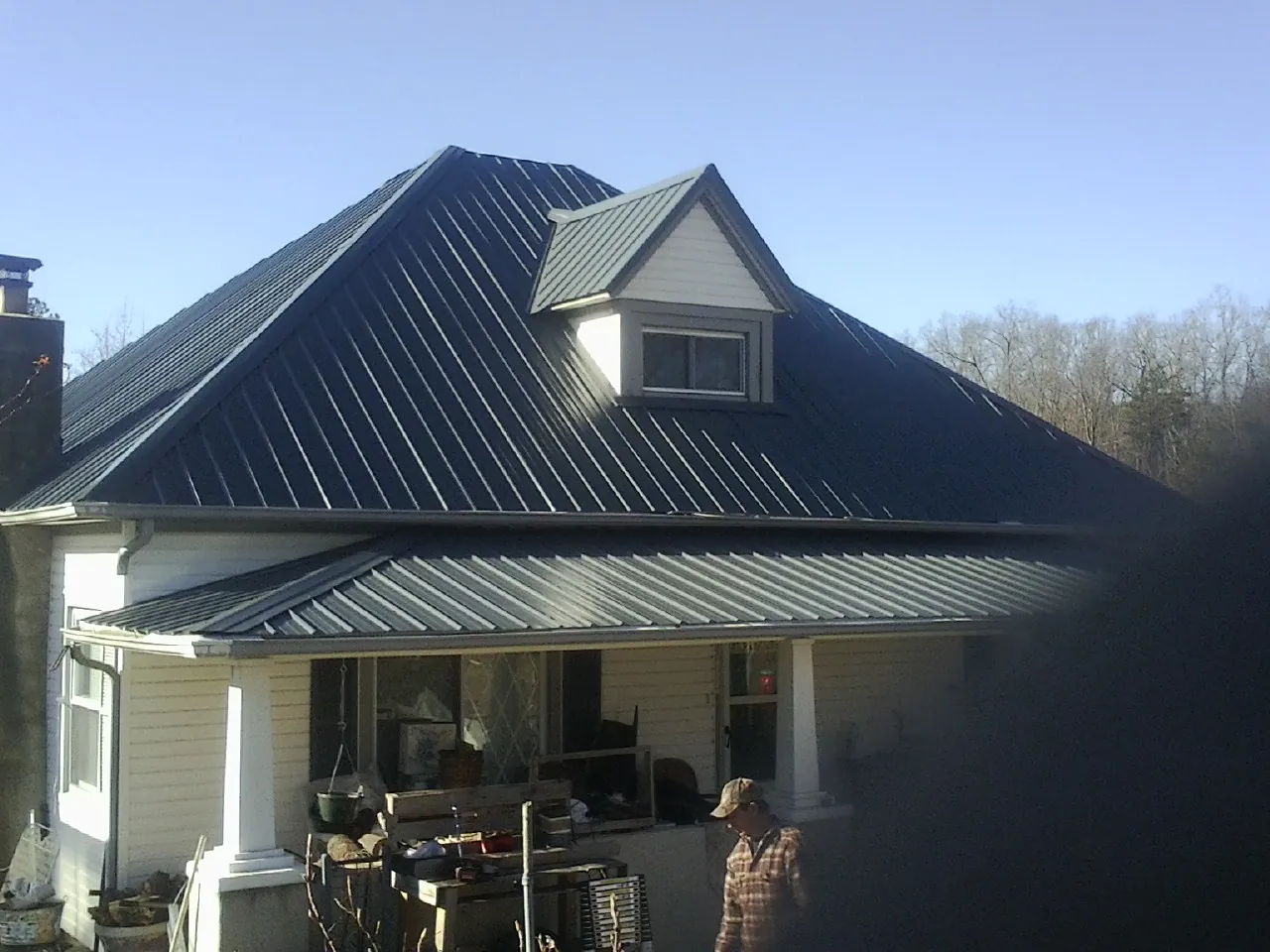 Dark blue standing seam metal roof with a dormer above a front porch in Leo