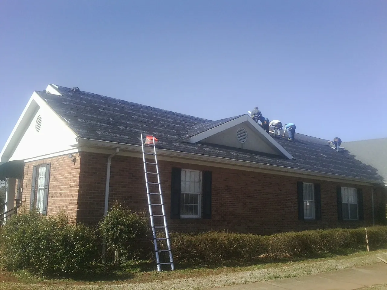 Crew tearing shingles off a brick ranch roof with a ladder set — Emergency Roof Repair work by our crew in Leo