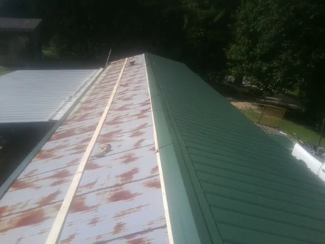 Old rusted panels beside newly installed green metal roofing — Wind Damage Roof Repair by Roofing Brothers in Leo