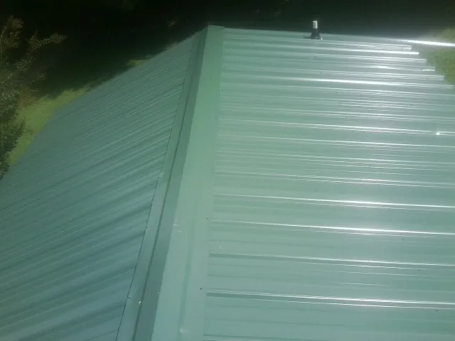New green metal panels meeting at the ridge of a roof — Flat Roof Repair work by our crew in Leo