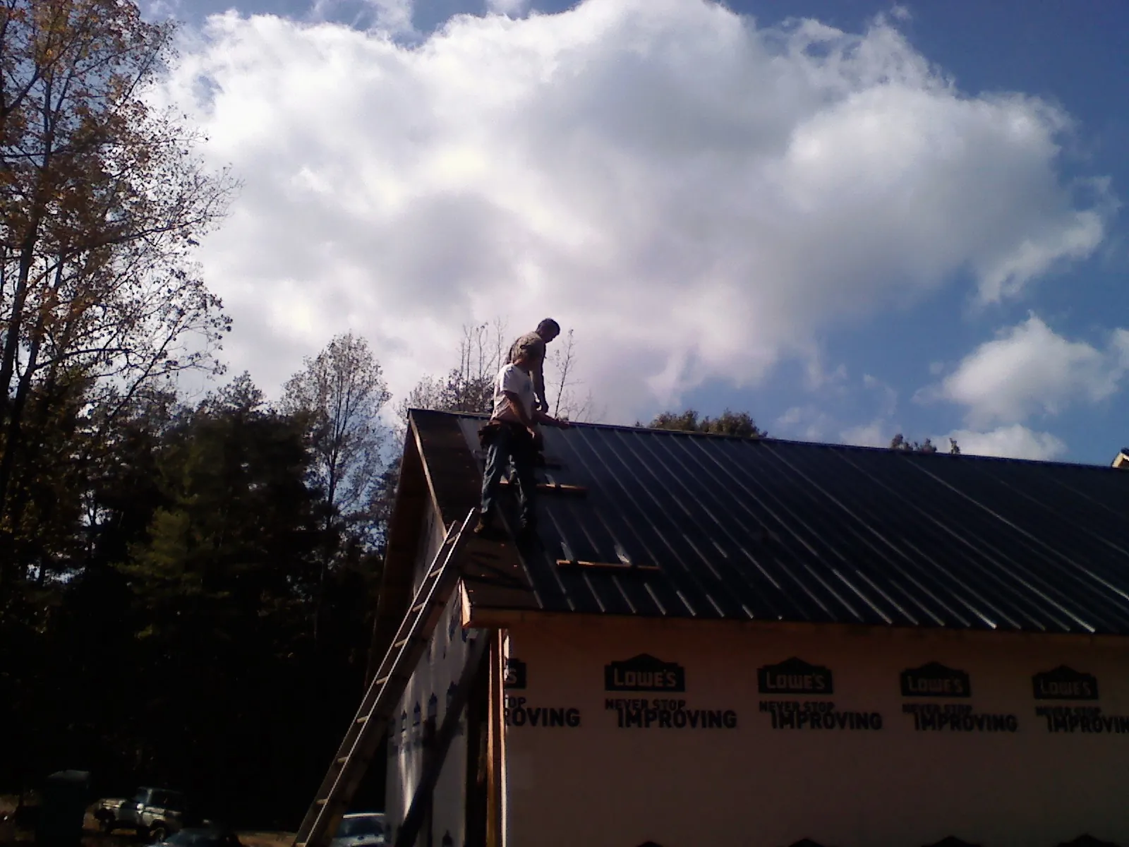 Roofer fastening dark metal panels high against a cloudy sky, from a Roof Inspection job in Leo