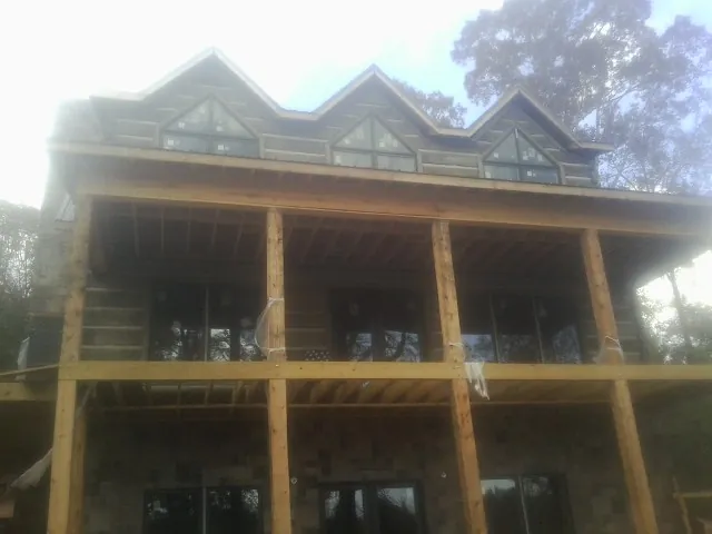Dormers and porch framing on a large log home under construction — Roof Coating work by our crew in Leo